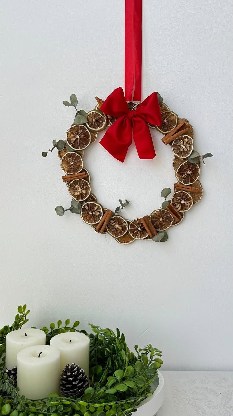 Dried orange and cinnamon wreath with red bow hanging on white wall