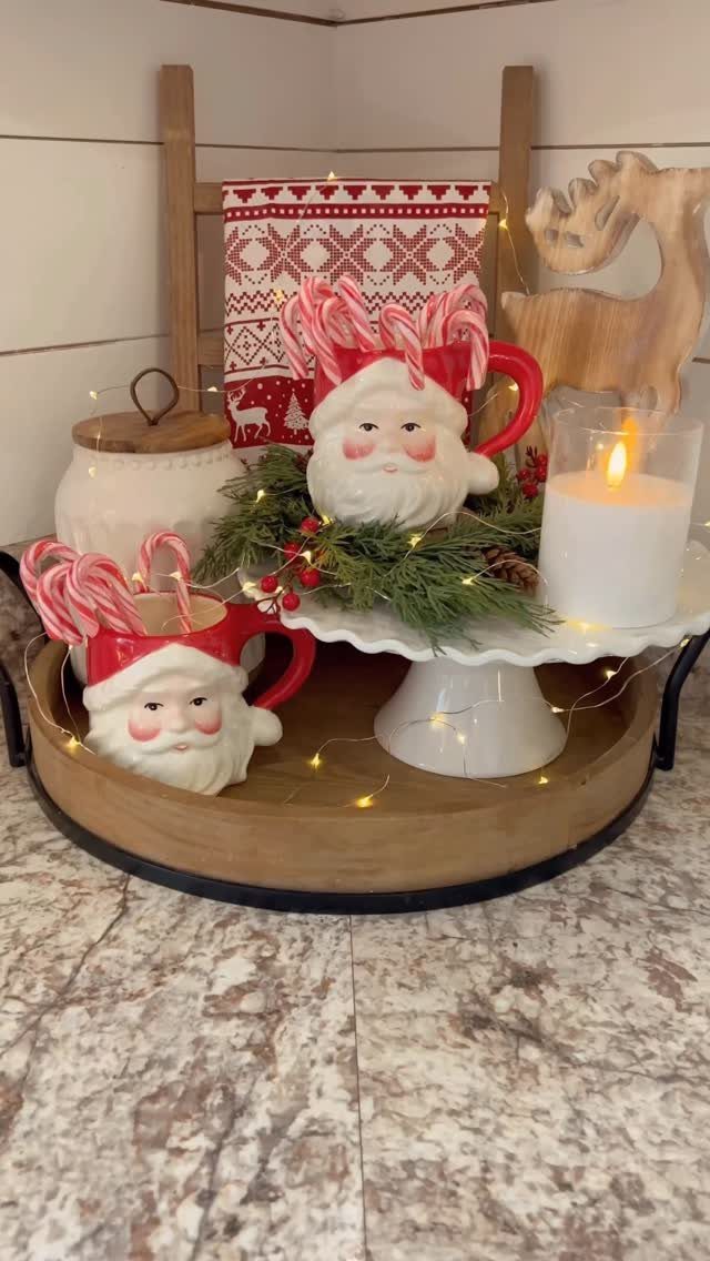 Santa Claus mugs with candy canes and a candle on a wooden tray.