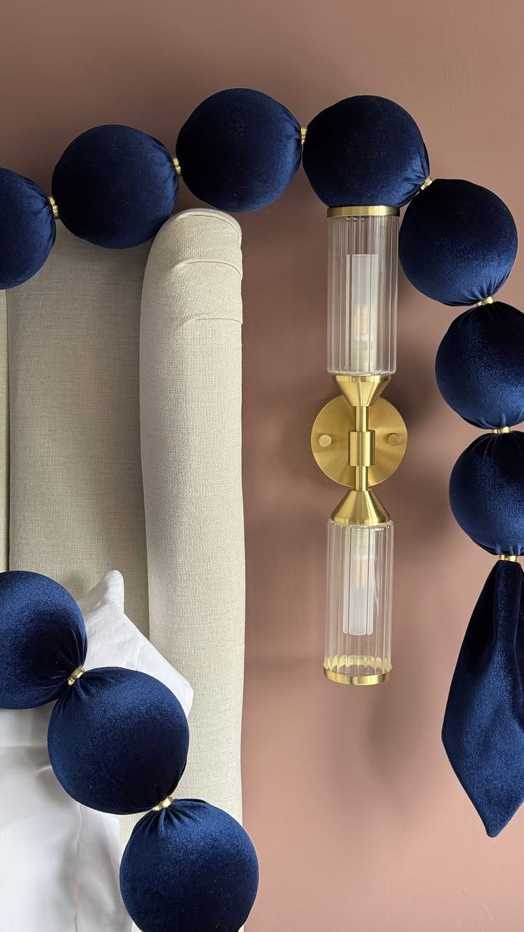 Navy blue velvet ball garland draped over a beige headboard and gold wall sconce.