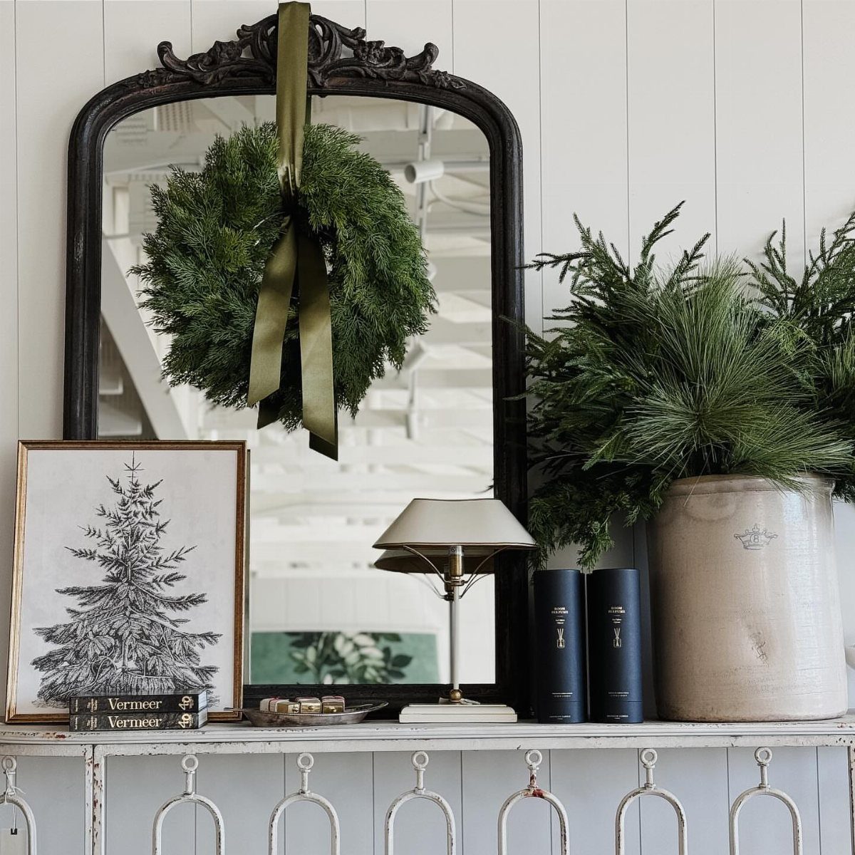 Green evergreen wreath with gold ribbon hanging on an ornate black mirror