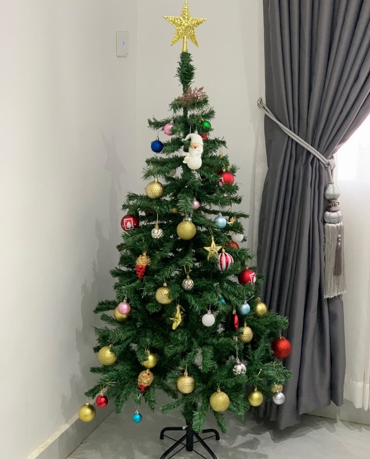 Decorated artificial Christmas tree with colorful ornaments and a gold star topper.