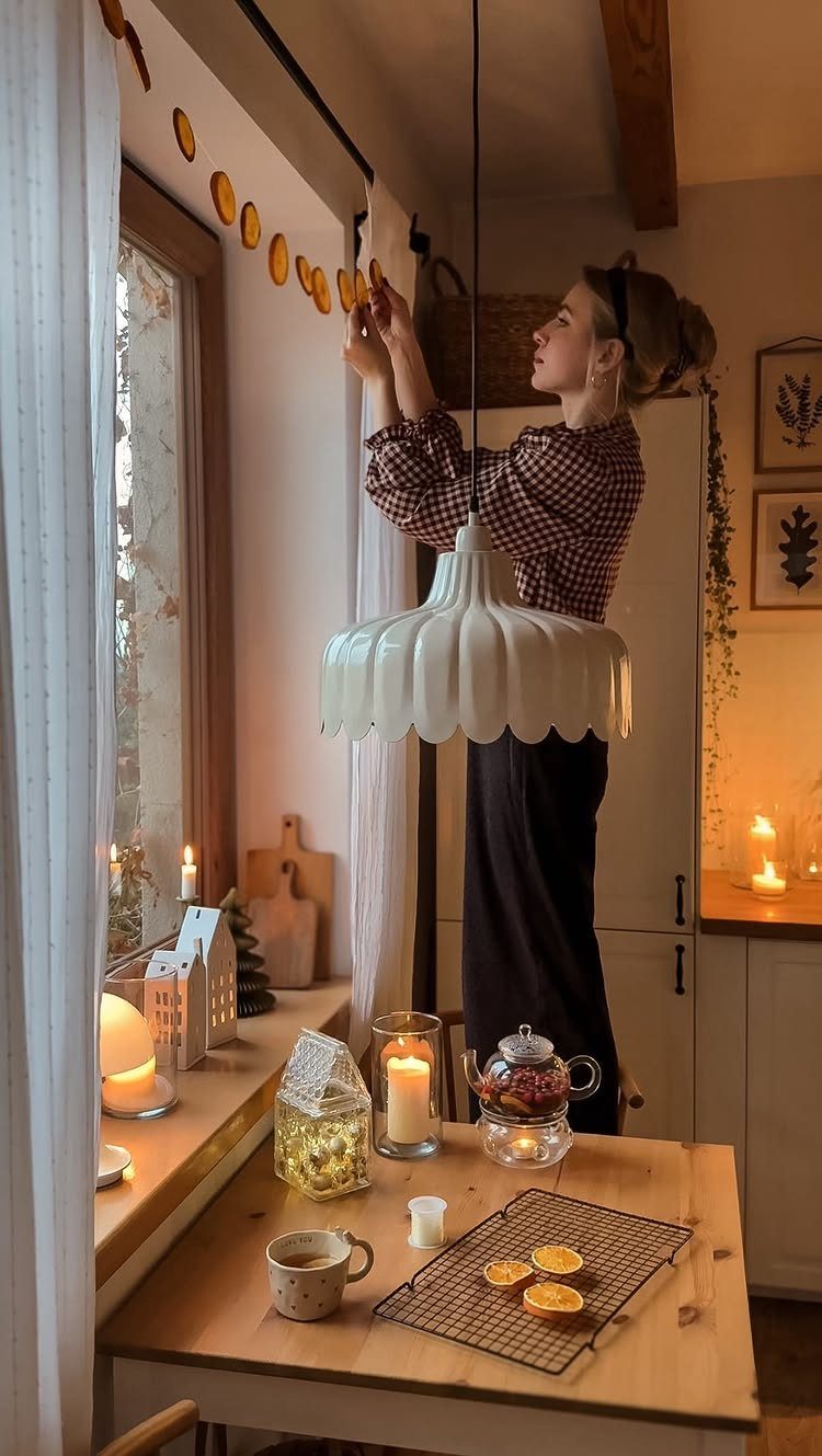 Woman hanging a dried orange slice garland across a window in a cozy kitchen