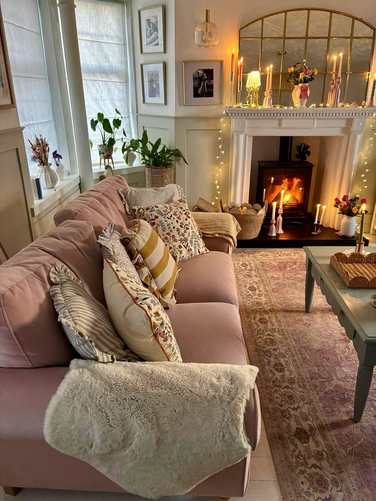 Cozy living room with pink sofa, glowing fireplace, and festive Christmas candle decorations.