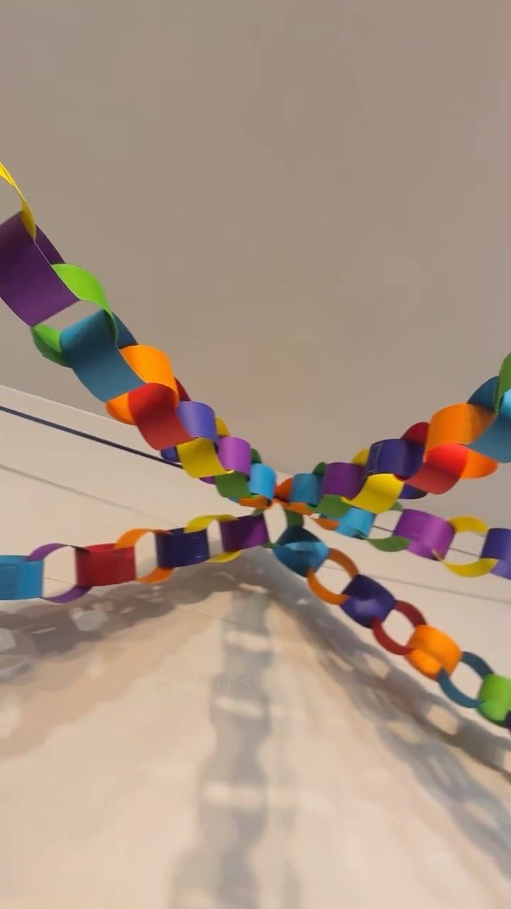 Colorful paper chain garlands hanging from a white ceiling with reflections below.