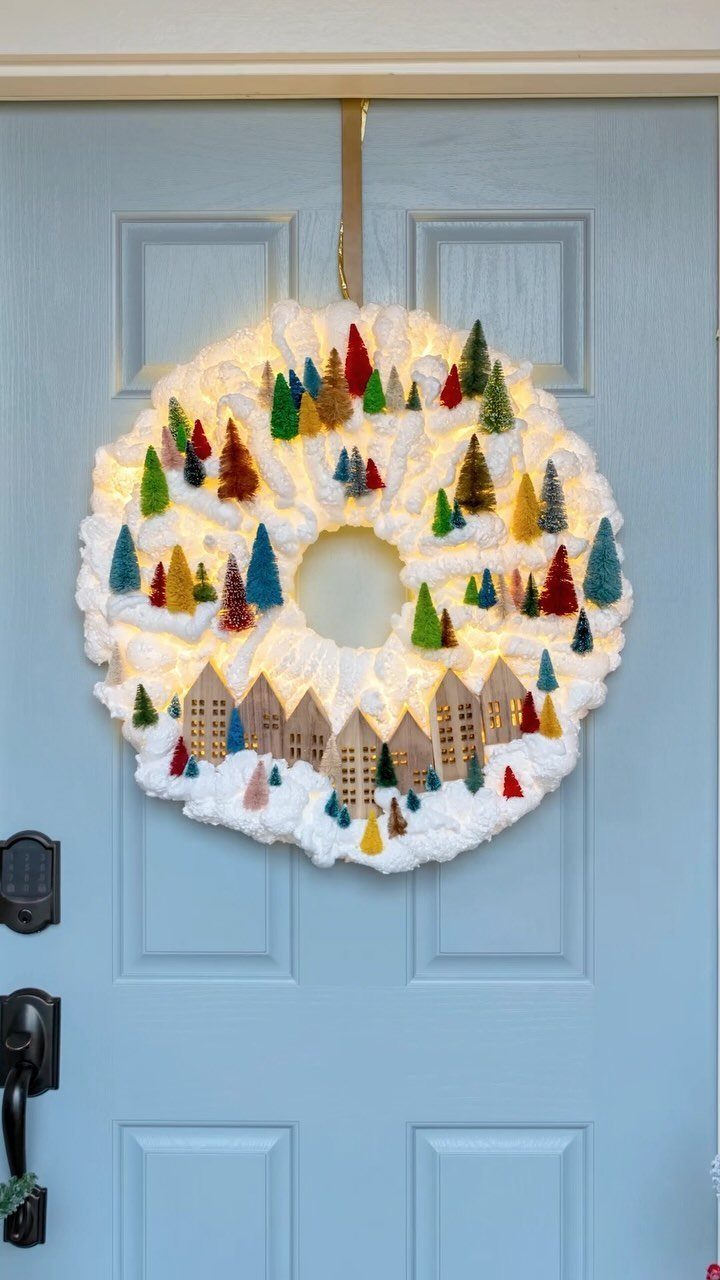 Snowy white wreath with miniature trees and houses hanging on a blue door