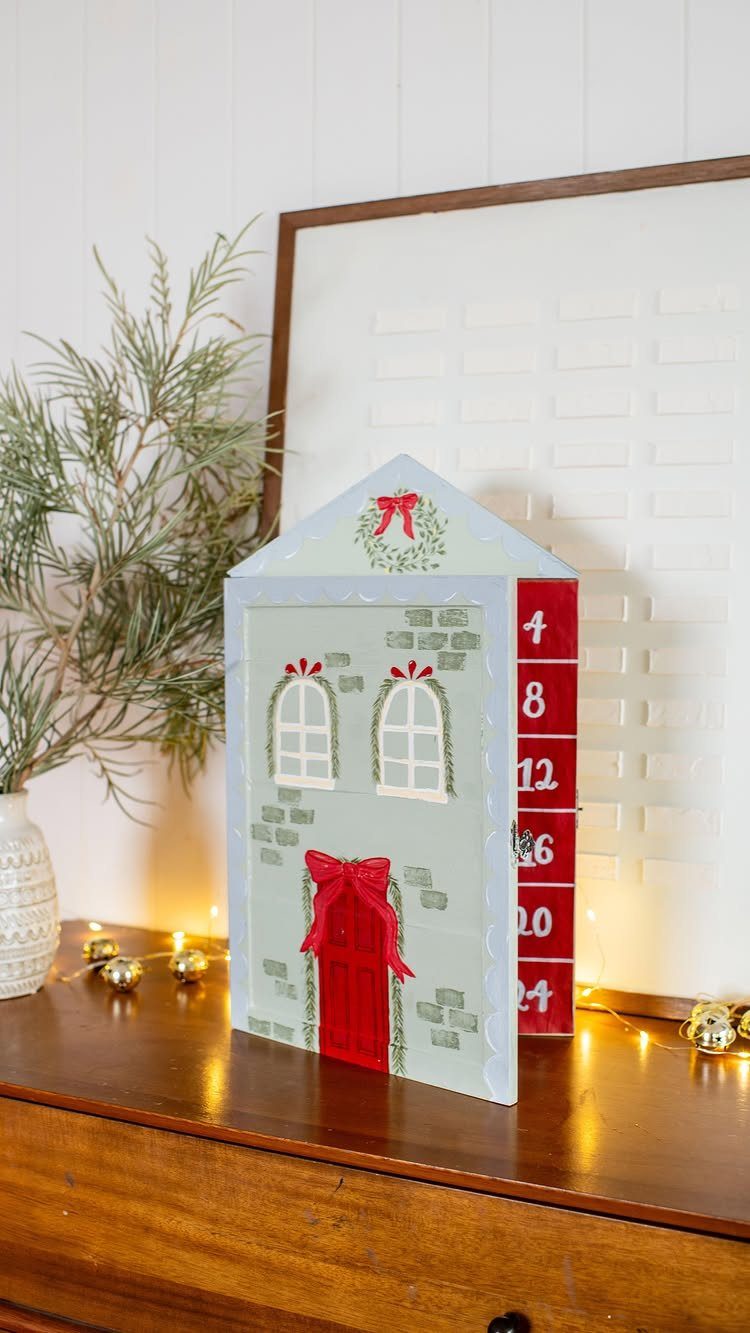 House-shaped blue advent calendar with red door and numbered drawers on wooden table