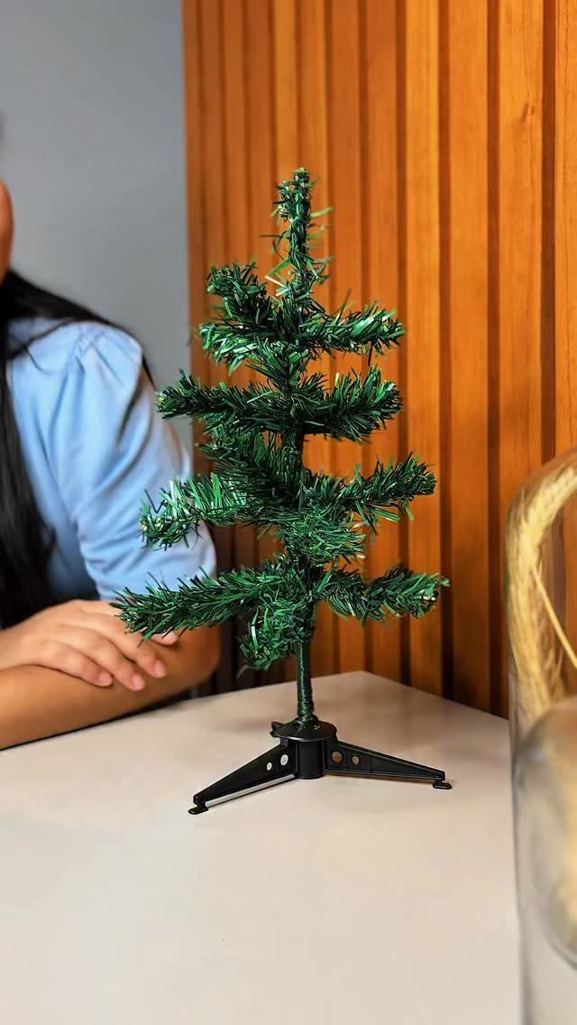 Small green artificial Christmas tree on a white table against wooden wall