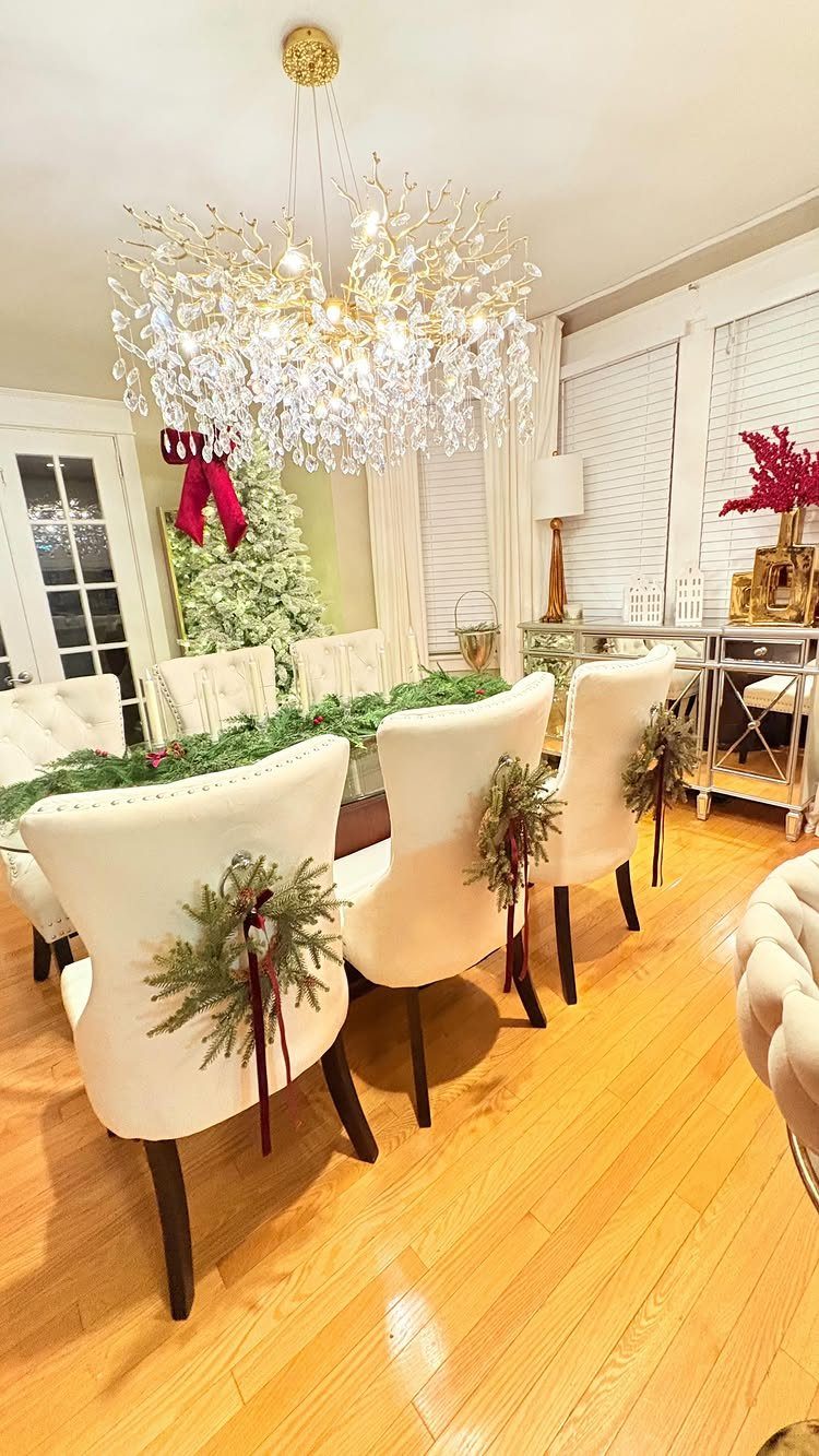 White dining chairs decorated with small evergreen wreaths and red ribbons in a room.