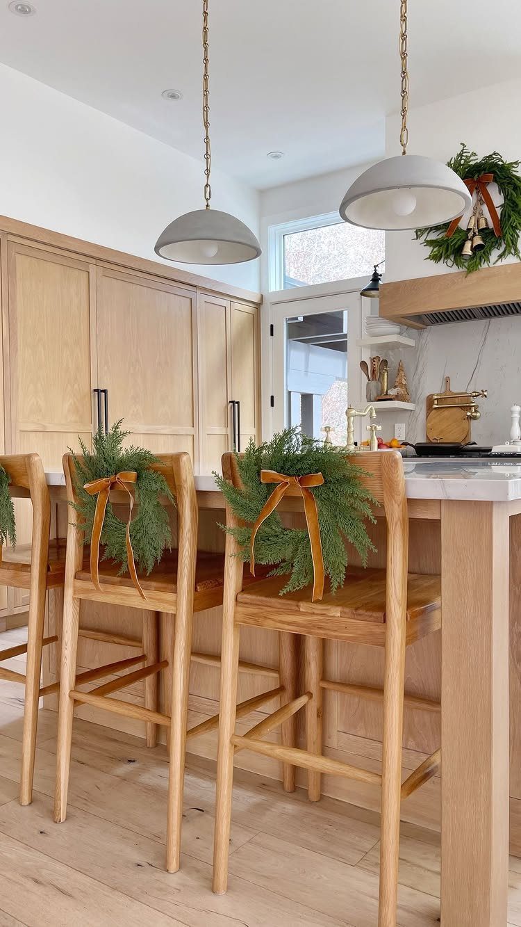 Wooden bar stools decorated with evergreen wreaths and orange ribbons in a kitchen