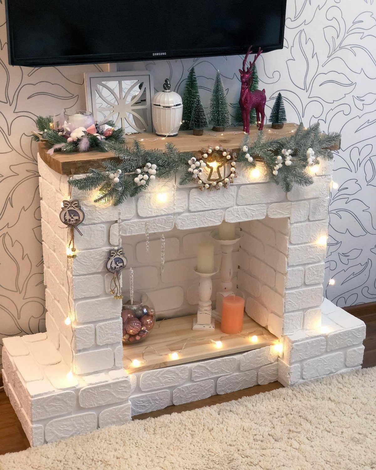 White faux brick fireplace mantel decorated with Christmas greenery and twinkle lights.