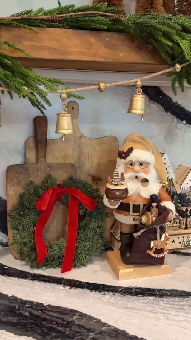 Santa figurine and a red-bowed wreath arranged with wooden boards under a shelf.