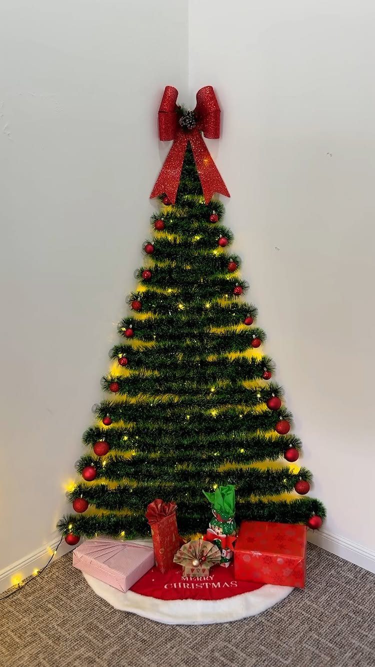 Tinsel Christmas tree with red bow and gifts placed in a white room corner.