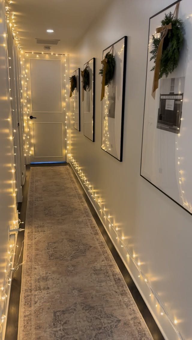 Narrow hallway decorated with warm string lights and small wreaths on framed art.
