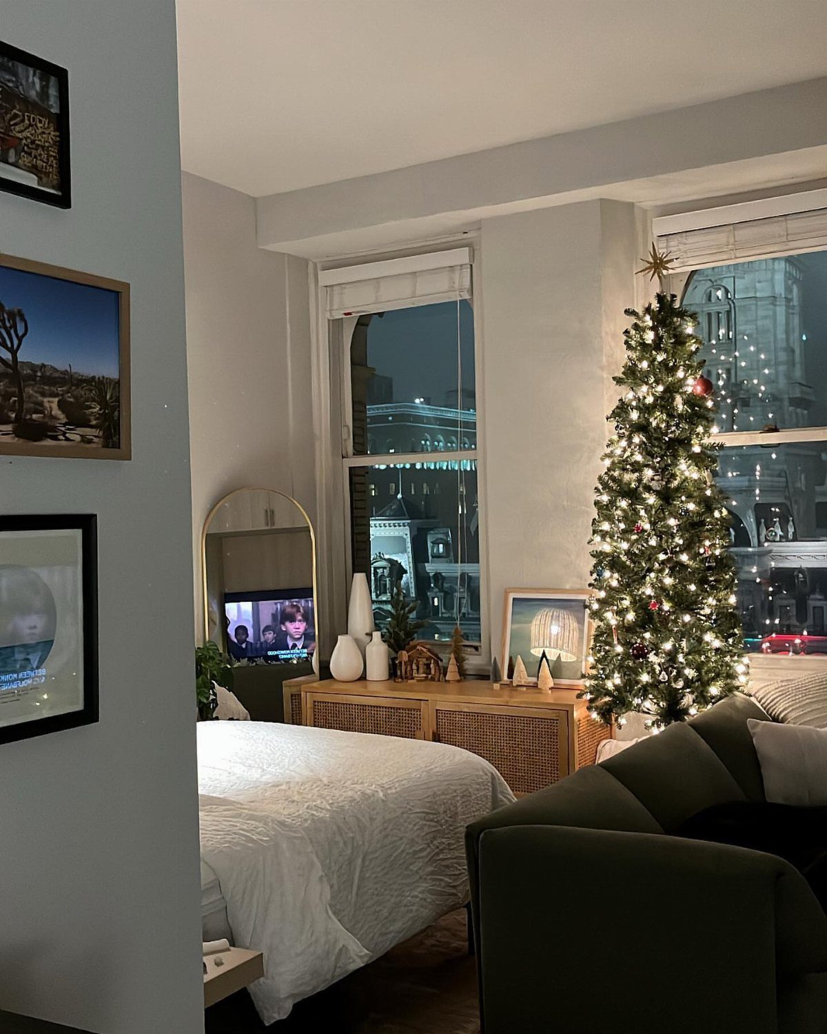 Lit Christmas tree and white bedding in a small, decorated studio apartment interior.