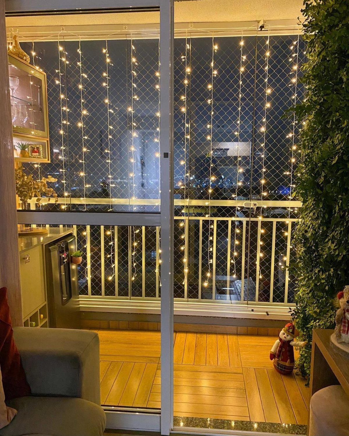 Wooden balcony decorated with curtain string lights and a small festive figure at night