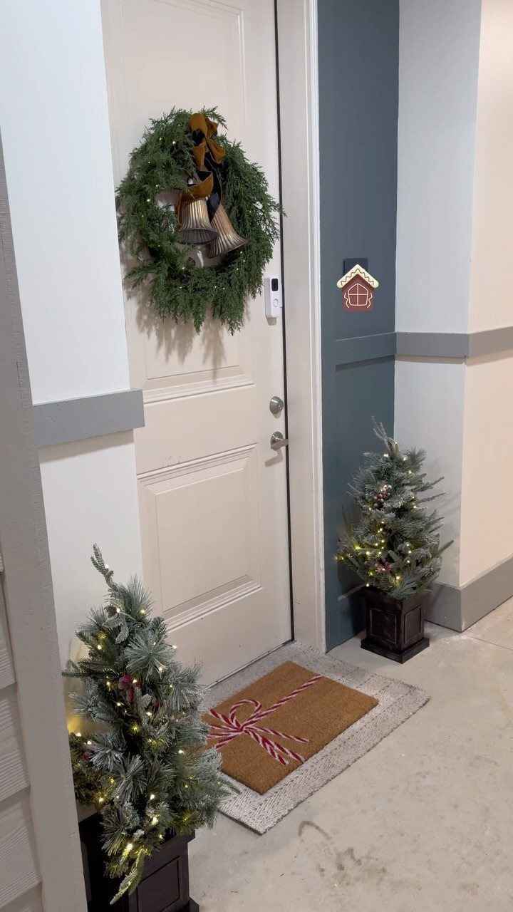Green evergreen wreath with bells hanging on a white door between two small trees