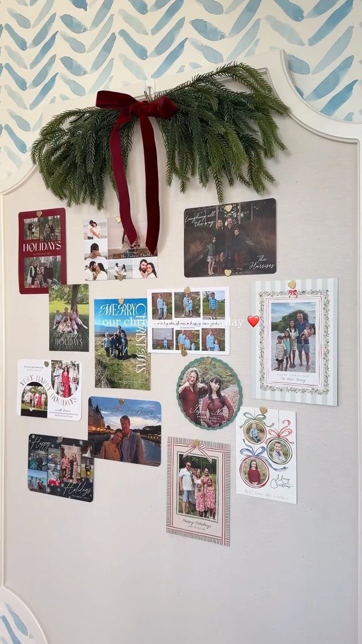 Christmas cards and photos pinned to a wall under a pine garland bow