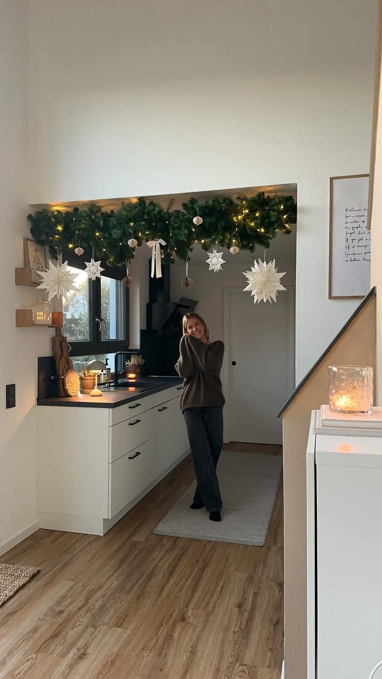 Woman standing in a kitchen with a festive pine garland and star ornaments.