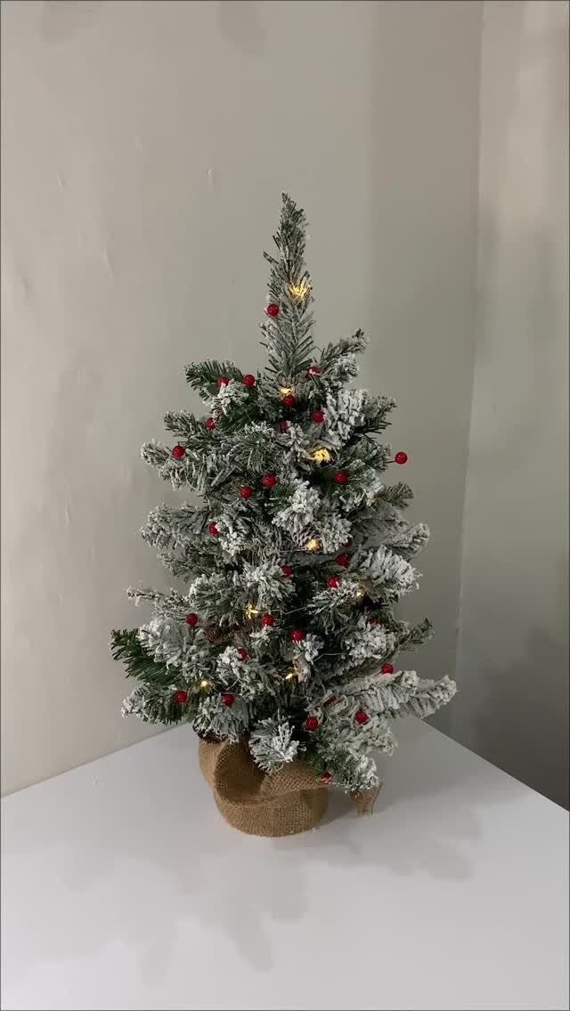 Small flocked Christmas tree with red berries and lights on a white table