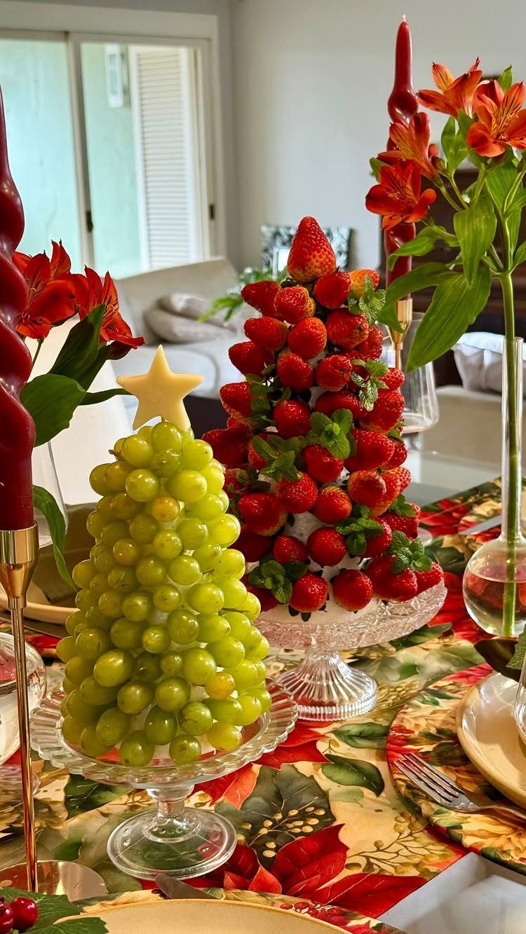 Fruit towers shaped like Christmas trees made of grapes and strawberries on a table.