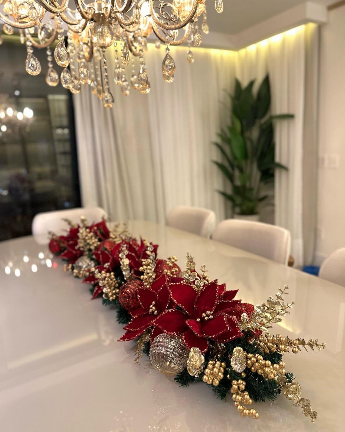 Christmas table centerpiece with red poinsettias and gold ornaments on a white table