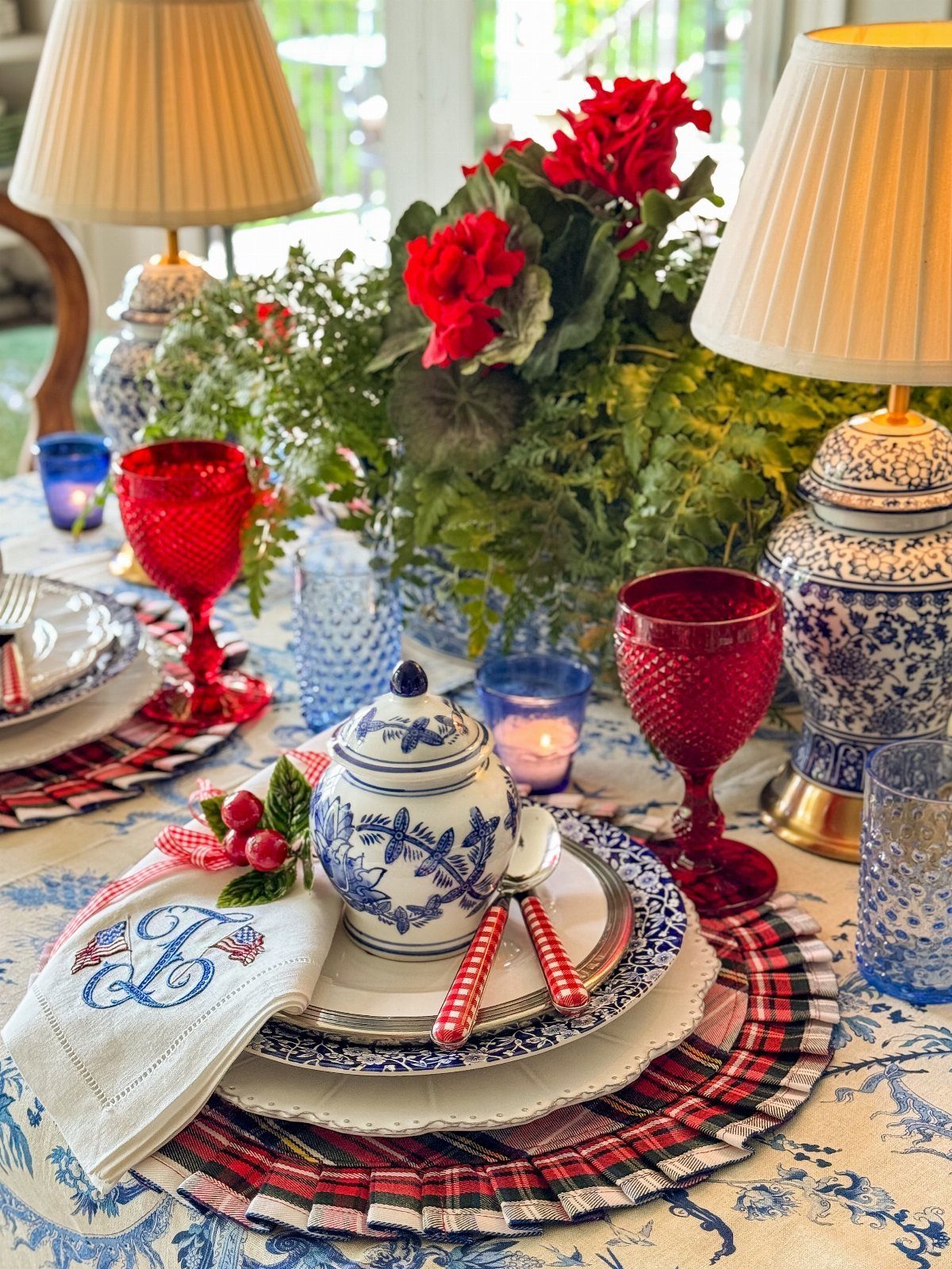 Festive table setting with red glassware, blue and white ceramics, and red floral centerpiece.