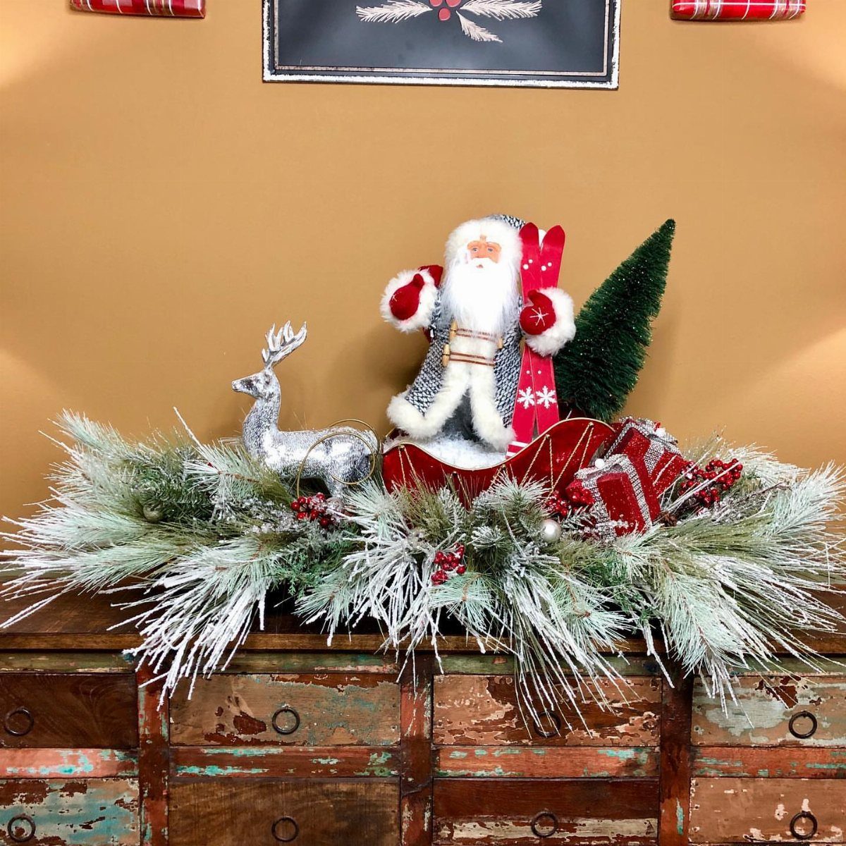 Santa in a red sleigh with a silver reindeer and frosted evergreen branches.