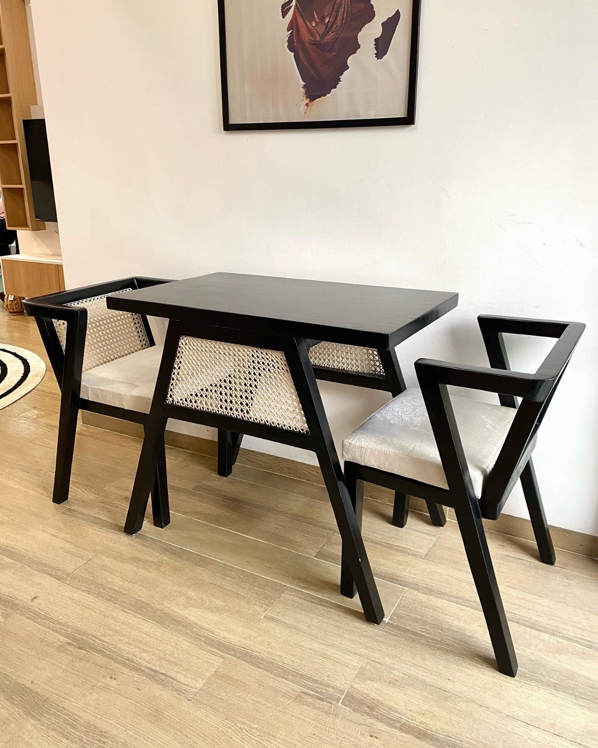 Black rectangular dining table with two matching chairs and woven cane backrests.
