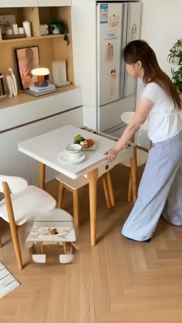 Small white square dining table with wooden legs and a drop-leaf side.