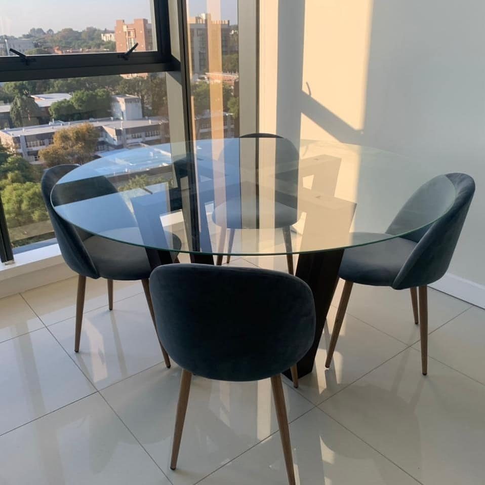 Round glass-top dining table with navy blue velvet chairs in a bright room.