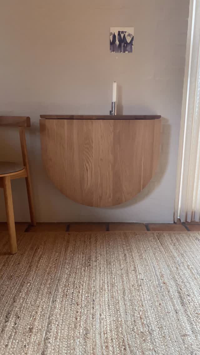 Semi-circular wooden wall-mounted table with a matching chair and woven jute rug.