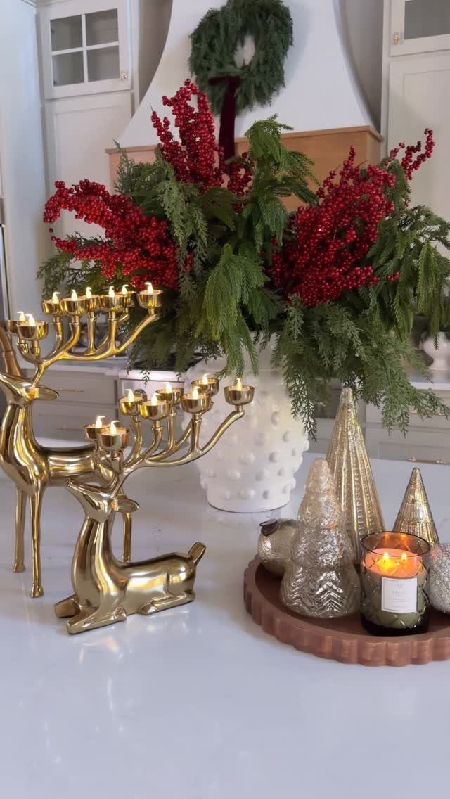 Green cedar branches and red berries in a white vase with gold deer candelabras.