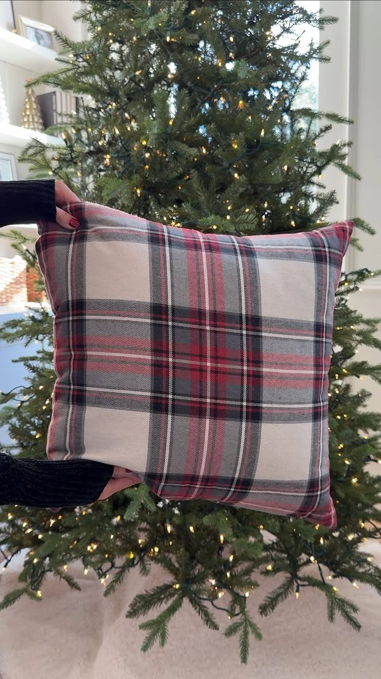 Plaid red and white holiday pillow held in front of a lit Christmas tree