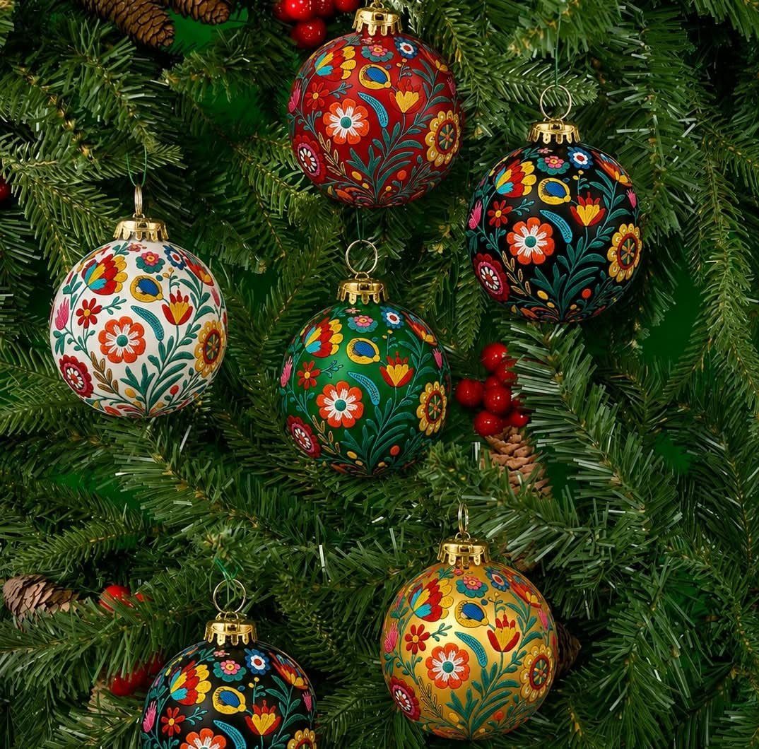 Floral painted Christmas ornaments hanging on a green pine tree with red berries.