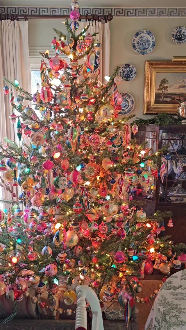 Decorated Christmas tree with colorful vintage glass ornaments and multi-colored lights in a room.