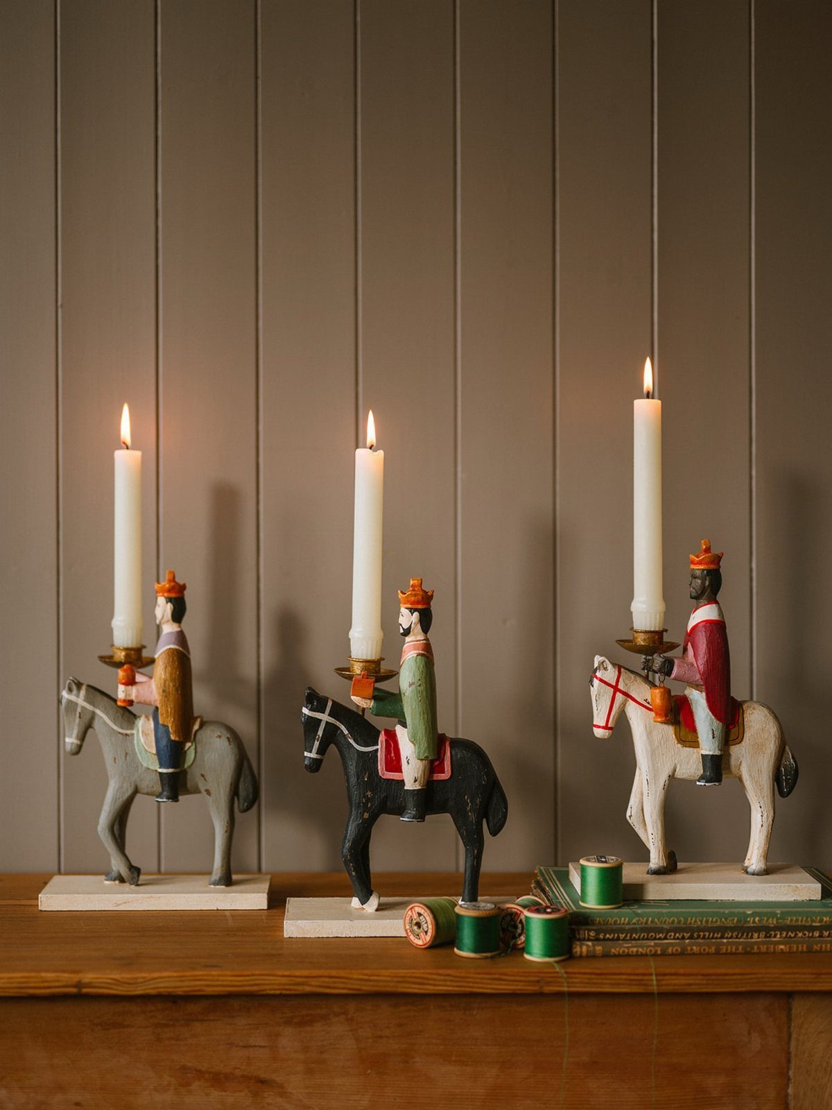 Three vintage wooden horse rider candle holders with lit white taper candles.