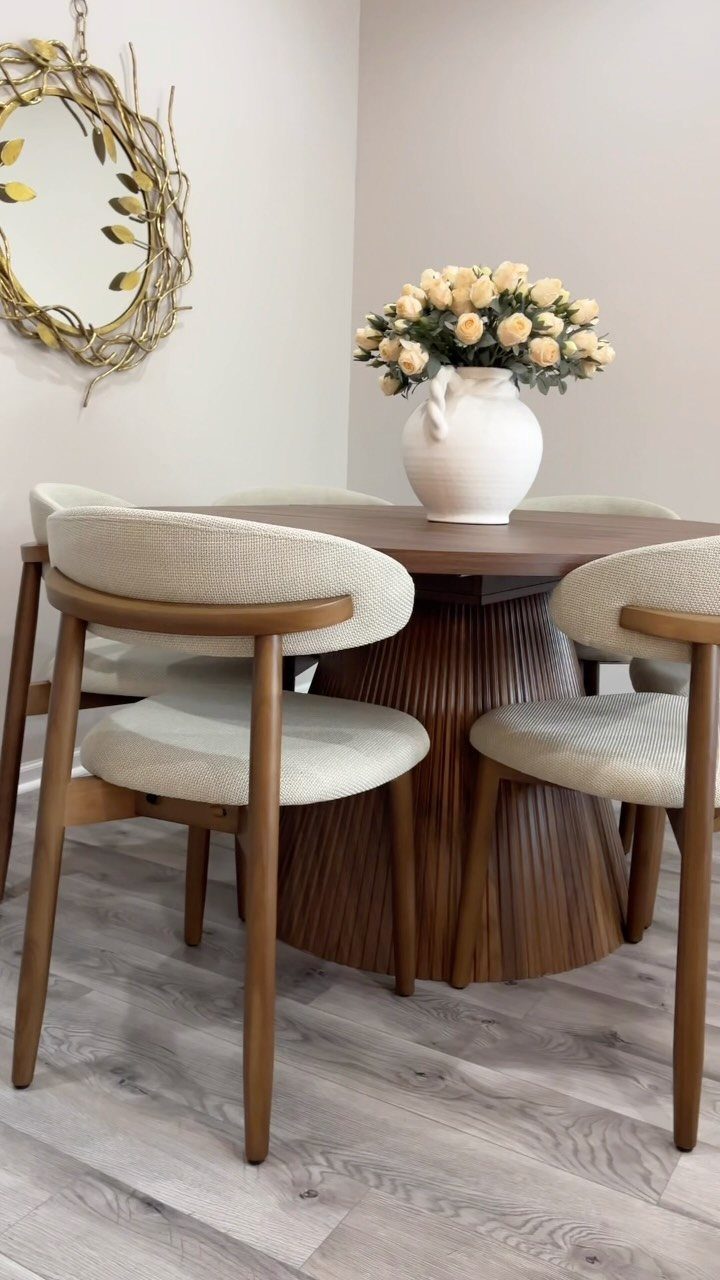 Round wooden dining table with fluted base and beige upholstered mid-century modern chairs.