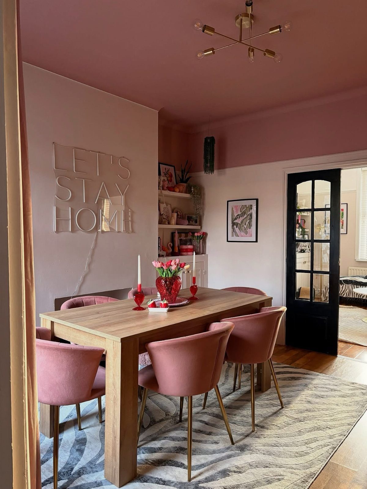 Wooden dining table with pink velvet chairs and gold accents in a modern room.