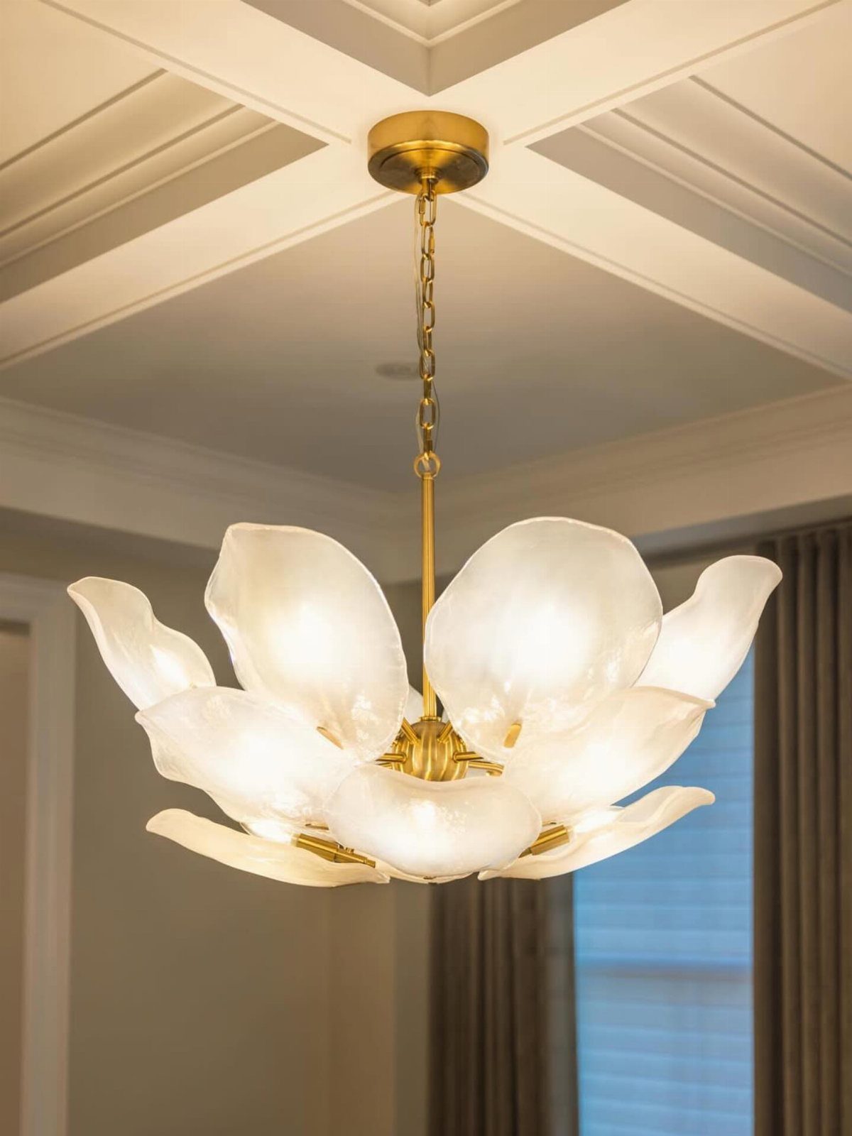 Gold flower-shaped chandelier with white glass petals hanging from a coffered ceiling.