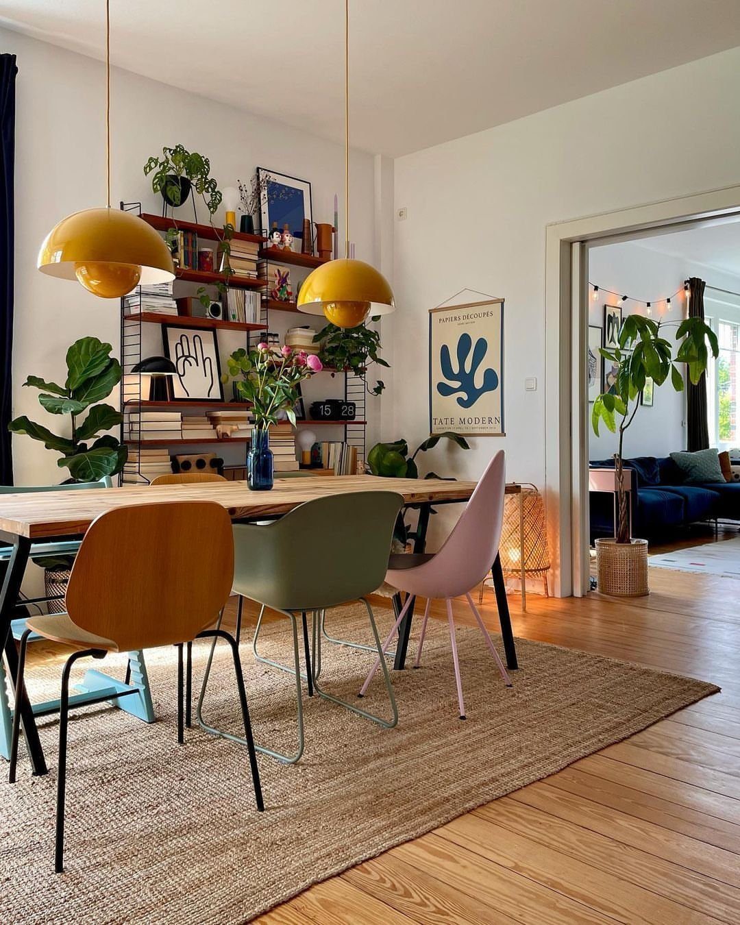Wooden dining table with eclectic mismatched chairs and yellow pendant lights in a room.