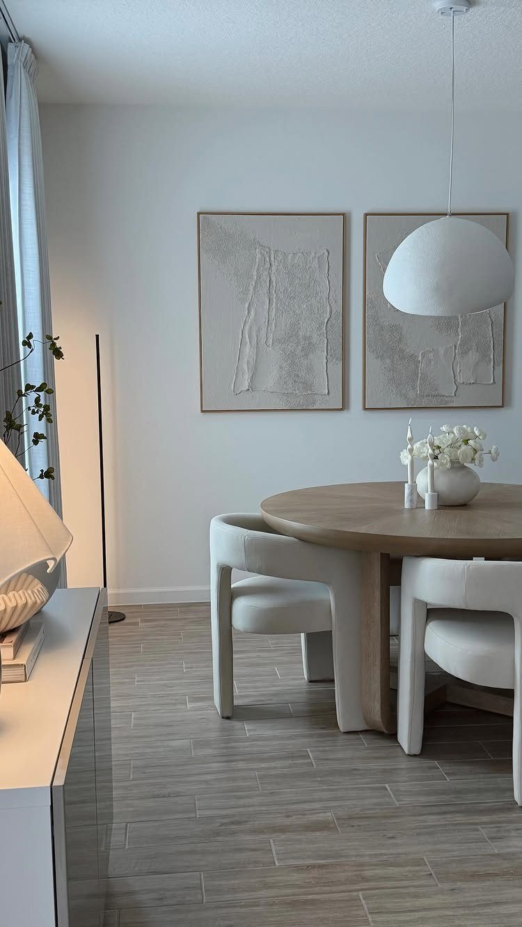 Round wooden dining table with white curved chairs and abstract wall art.