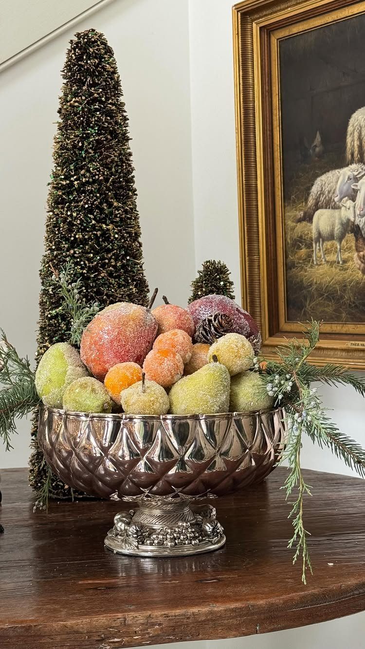 Frosted fruit in a silver bowl with pine branches and a conical topiary.