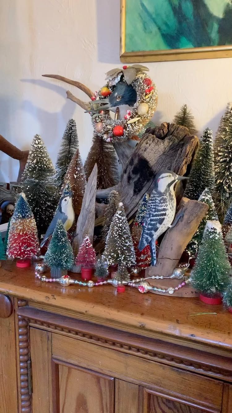 Bottle brush Christmas trees and bird figurines arranged on a wooden sideboard.