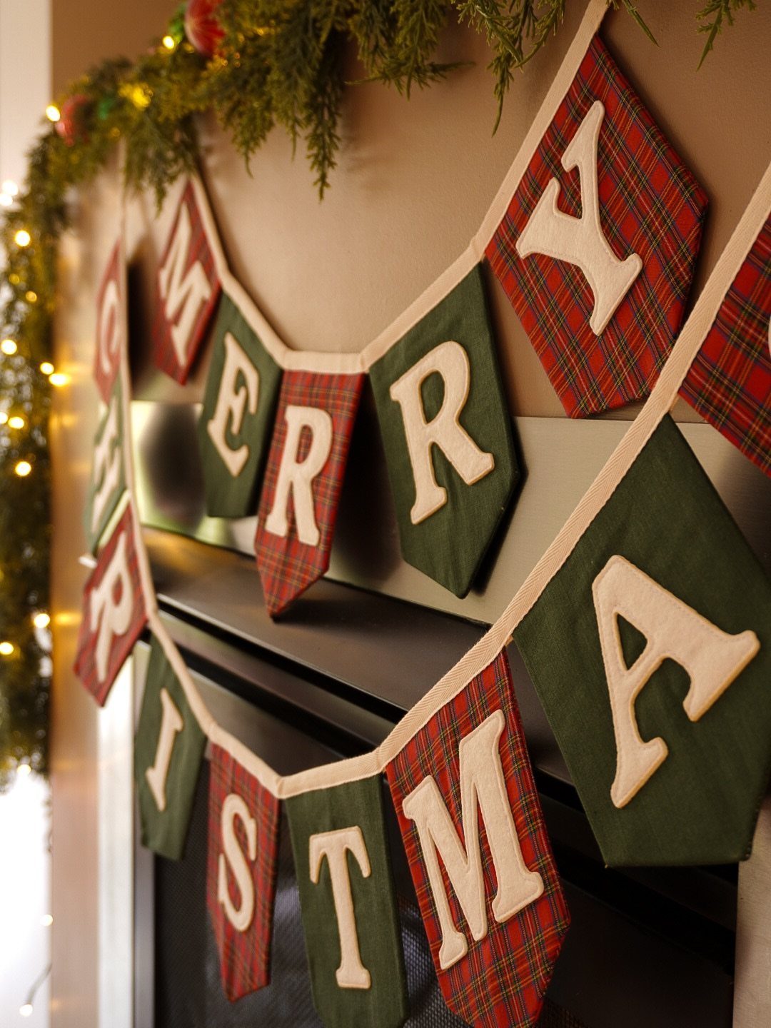 Fabric Merry Christmas banner with red plaid and green pennants under a lit garland.