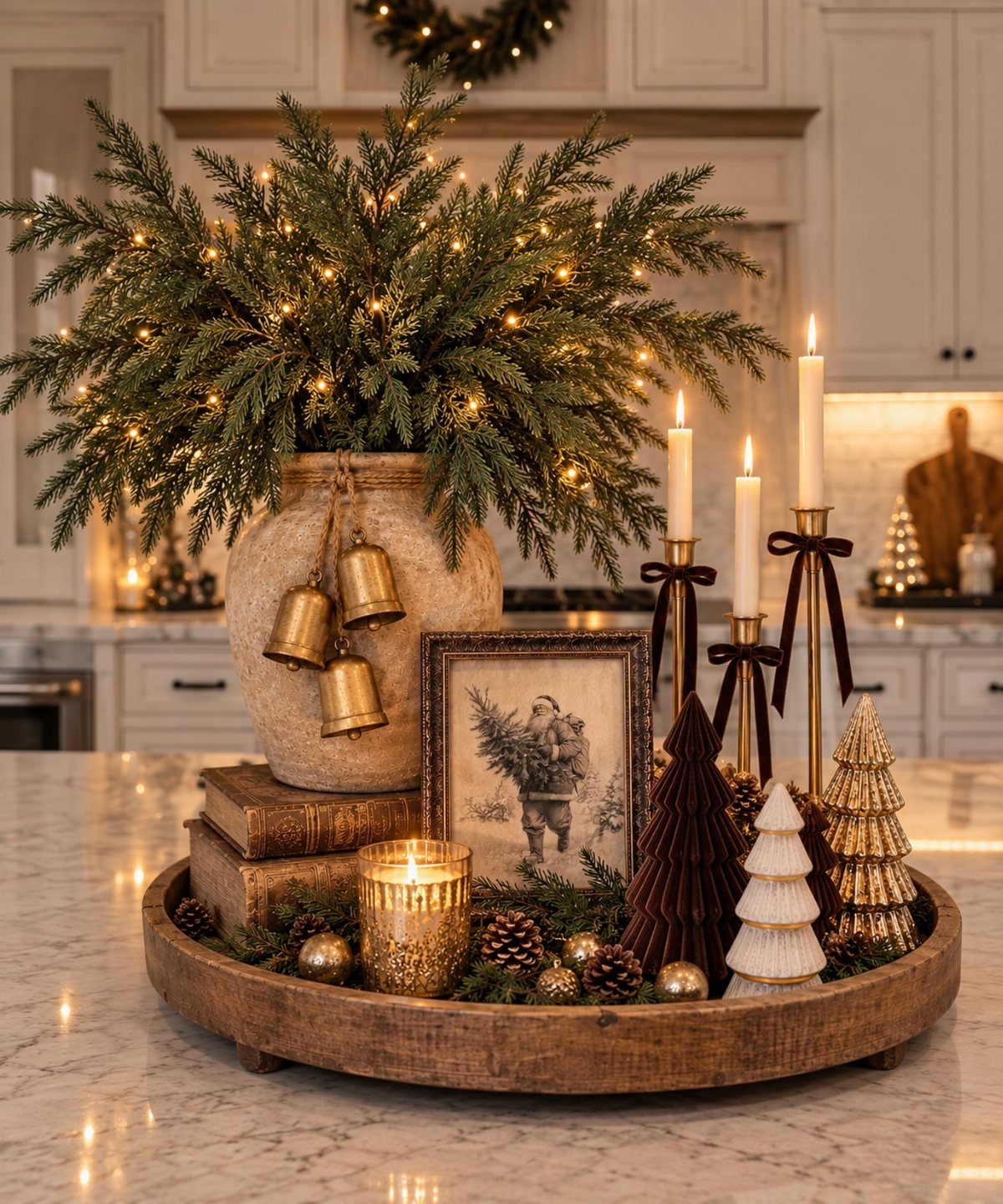 Holiday centerpiece with evergreen branches, gold bells, candles, and miniature trees on a tray.