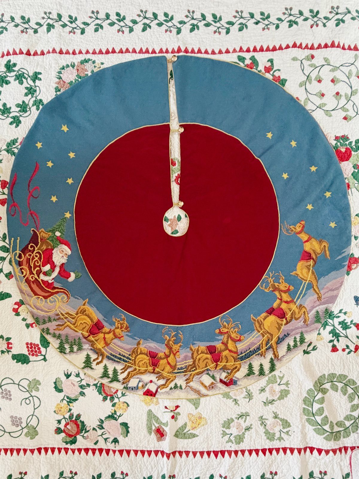 Circular blue and red Christmas tree skirt with embroidered Santa and reindeer scene.
