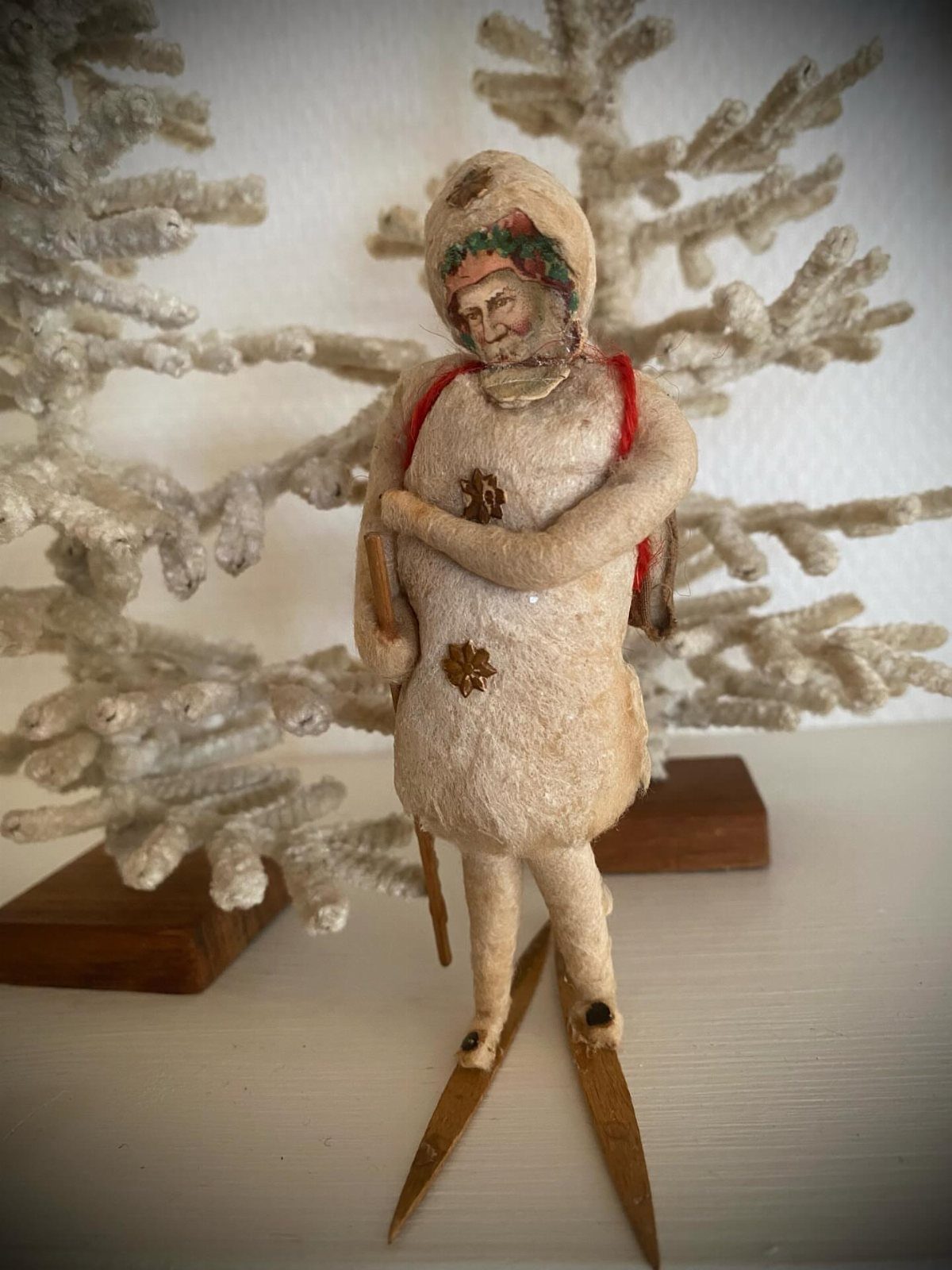 Vintage skier figurine in white winter gear standing on wooden skis before frosted tree