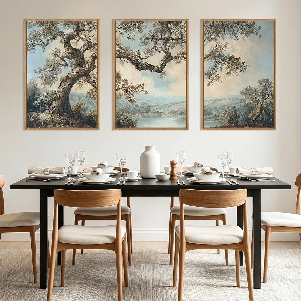 Three framed landscape paintings of trees hanging above a modern dining room table.