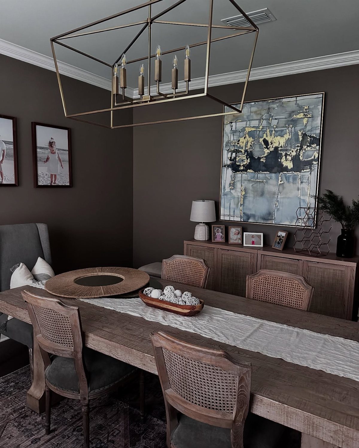 Dining room with cocoa brown walls, wooden table, and gold geometric chandelier.