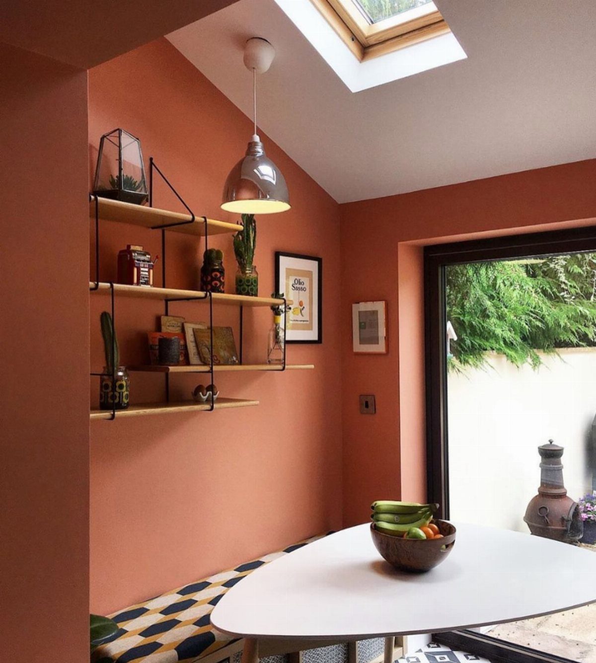 Terracotta walls in a dining room with a white table and wooden shelves.